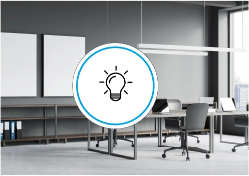 Helles modernes B&uuml;ro mit Schreibtischen und St&uuml;hlen, an der Decke h&auml;ngende Leuchten, im Vordergrund ein Symbol mit Gl&uuml;hbirne.