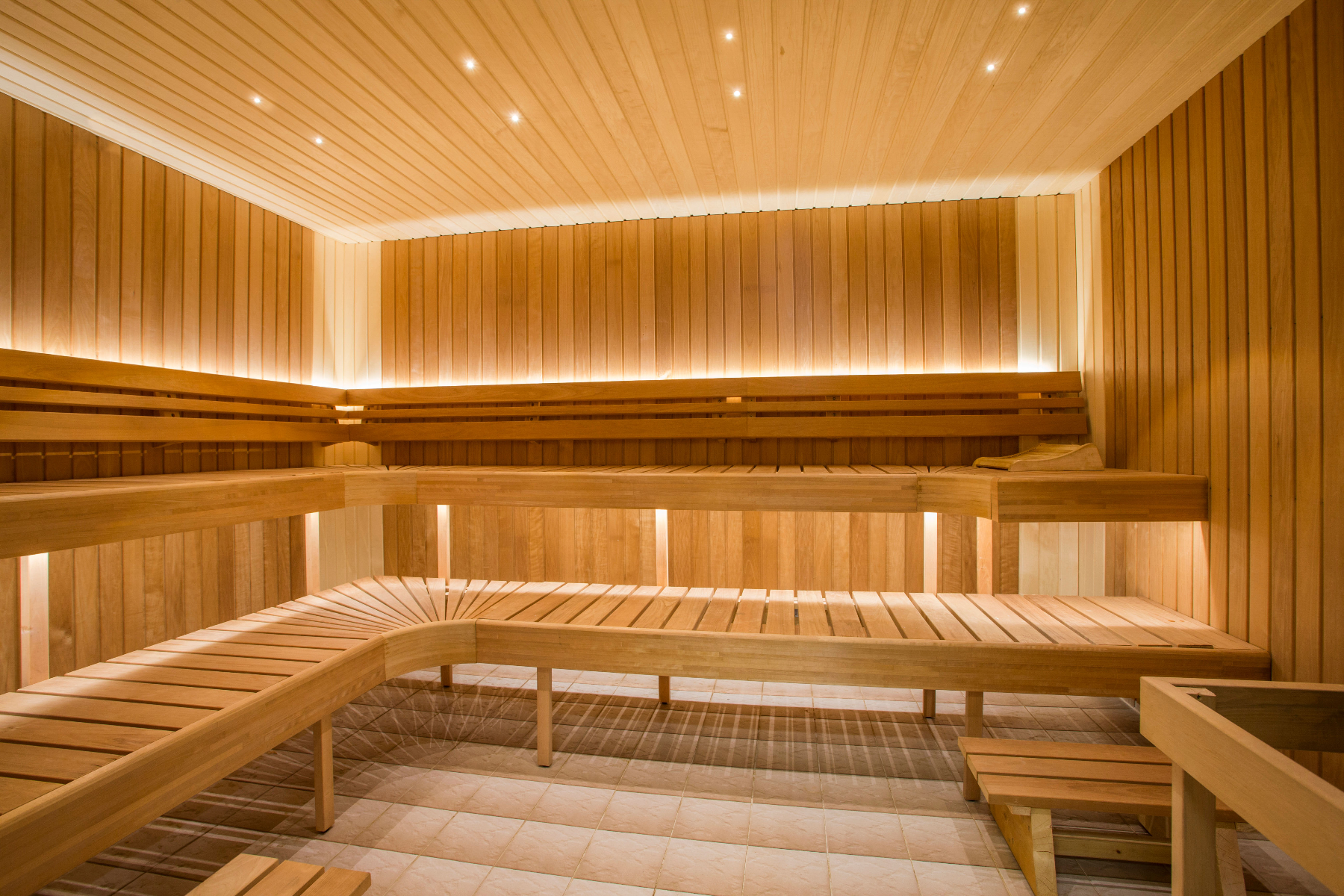 Panche in legno si trovano in un&rsquo;ampia sauna, illuminata da luci integrate e soffuse. L&rsquo;ambiente &egrave; caldo e accogliente, con pareti in legno e pavimento piastrellato.